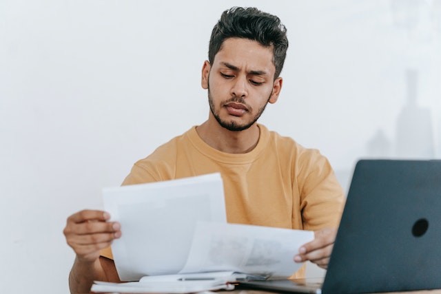 a-property-manager-in-a-yellow-sweater-reviews-documents-at-their-desk-with-a-laptop-nearby